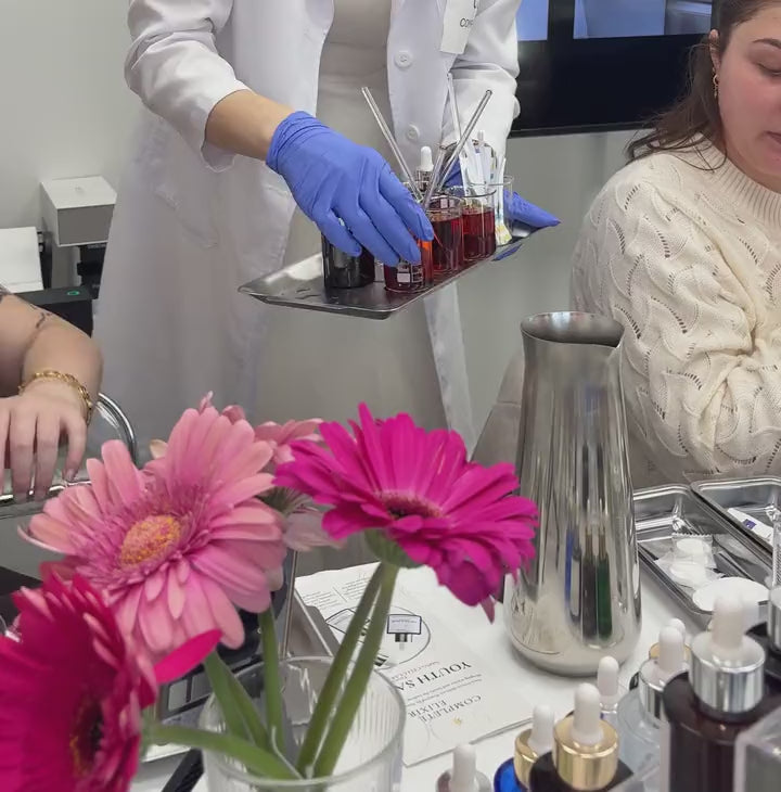Gloved hands preparing beakers of infusion on a tray, flowers in front